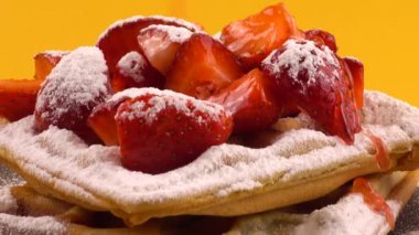 Çilekli Belçika waffleları, tatlı çilek sosu ve turuncu arka plandaki taş bir tahtada pudra şekeri..