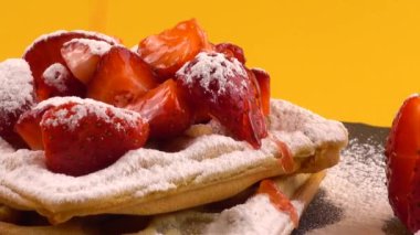 Çilekli Belçika waffleları, tatlı çilek sosu ve turuncu arka plandaki taş bir tahtada pudra şekeri..