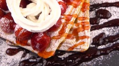 Çilekli Belçika waffleları, tatlı çilek soslu, krem şantili ve pudra şekerli beyaz arka planda bir taş tahtada.