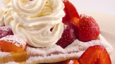 Çilekli Belçika waffleları, krema ve pudra şekerli beyaz bir arka planda..