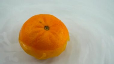 Beyaz bir zemin üzerinde olgun turuncuyu suyla döndürüyor. Yavaş çekim.