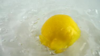 Beyaz bir zemin üzerinde olgun limonu suyun içinde döndürmek. Yavaş çekim.