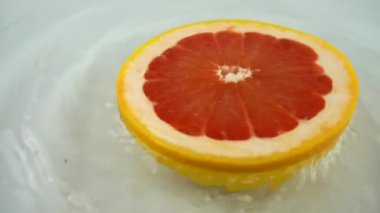 Beyaz zemin üzerinde olgun ve sulu greyfurt parçalarını döndürerek. Yavaş çekim.