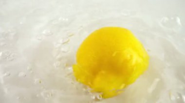 Beyaz bir zemin üzerinde olgun limonu suyun içinde döndürmek. Yavaş çekim.