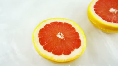 Beyaz bir zemin üzerinde olgun ve sulu greyfurt parçalarını döndürerek. Yavaş çekim.