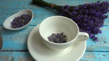 Eski ahşap arka planda taze lavanta çiçeklerinin çayı. Çay, sıcak suda bir bardakta demlenir. Kaynar su bir fincan çaya dökülür. Yavaş çekim.