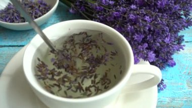 Eski ahşap arka planda taze lavanta çiçeklerinin çayı. Çay, sıcak suda bir bardakta demlenir. Yavaş çekim.