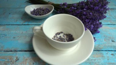Eski ahşap arka planda taze lavanta çiçeklerinin çayı. Çay, sıcak suda bir bardakta demlenir. Kaynar su bir fincan çaya dökülür. Yavaş çekim.