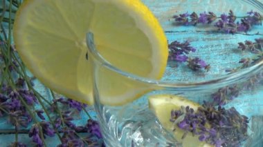 Taze lavanta çiçeklerinden limonata ve ahşap bir arka planda limon hazırlamak. Düşen buz parçaları ve akan su bir bardağa dökülür..