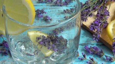 Taze lavanta çiçeklerinden limonata ve ahşap bir arka planda limon hazırlamak. Düşen buz parçaları ve akan su bir bardağa dökülür..