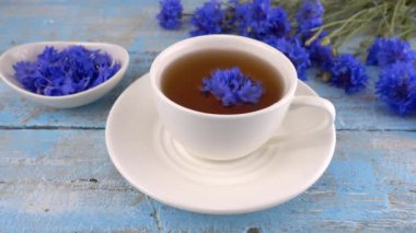 Composition with knapweeds flowers in white and blue colors on vintage light blue wooden tabletop. Brewing a tisanes from knapweeds flowers in white cup.