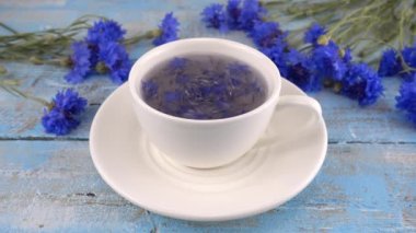 Composition with knapweeds flowers in white and blue colors on vintage light blue wooden tabletop. Brewing a tisanes from knapweeds flowers in white cup.
