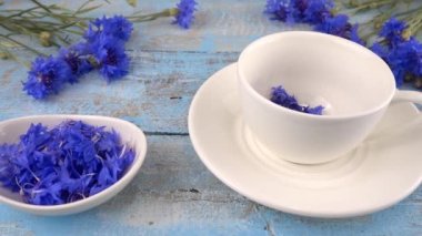 Composition with knapweeds flowers in white and blue colors on vintage light blue wooden tabletop. Brewing a tisanes from knapweeds flowers in white cup.