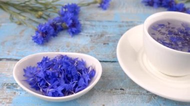 Knapweed çiçekli kompozisyon beyaz ve mavi renkte açık mavi ahşap masa üstünde. Knapweed 'lerden demlenen çiçekler beyaz bardakta.