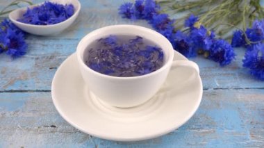 Composition with knapweeds flowers in white and blue colors on vintage light blue wooden tabletop. Brewing a tisanes from knapweeds flowers in white cup.
