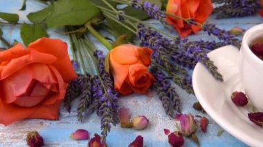 Provencal style composition: tea with fragrant rose buds, fresh rose flowers and lavender on a vintage light blue wooden tabletop.