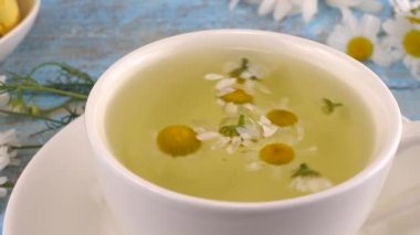 Papatya çiçekleri, bitki çayı ve klasik açık mavi ahşap masa üstünde badem kurabiyesi kompozisyonu. Papatya çayını beyaz fincanda demliyorum. Yaz teması.