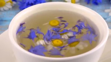 Composition with fresh knapweeds, chamomile flowers and herbal tea on vintage light blue wooden tabletop. Brewing a tisanes from knapweeds and chamomile in white cup.