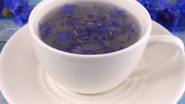 Composition with knapweeds flowers in white and blue colors on vintage light blue wooden tabletop. Brewing a tisanes from knapweeds flowers in white cup.