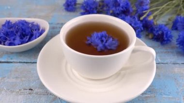 Composition with knapweeds flowers in white and blue colors on vintage light blue wooden tabletop. Brewing a tisanes from knapweeds flowers in white cup.