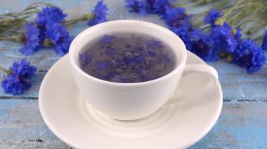 Composition with knapweeds flowers in white and blue colors on vintage light blue wooden tabletop. Brewing a tisanes from knapweeds flowers in white cup.