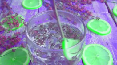 Taze lavanta çiçeklerinden limonata ve ahşap bir arka planda limon hazırlamak. Ağır çekim. İçeceğin hazırlanma aşamalarına bağlı olarak soyut arkaplan renk değişimi.