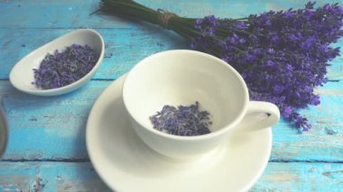 Eski ahşap arka planda taze lavanta çiçeklerinin çayı. Çay, sıcak suda bir bardakta demlenir. Kaynar su bir fincan çaya dökülür. Yavaş çekim.