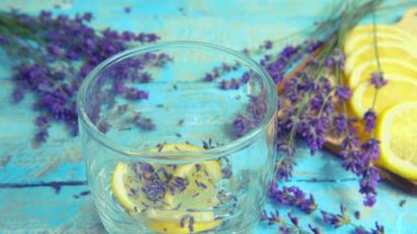 Taze lavanta çiçeklerinden limonata, ahşap bir arka planda limon. Düşen buz parçaları ve akan su bir bardağa dökülür. Yavaş çekim.