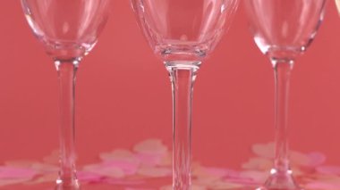 Köpüklü şarap, kalp şeklindeki konfetilerle pembe arka planda bardaklara dökülür..