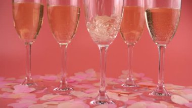 Pouring sparkling wine into glasses on a pink background with heart-shaped confetti. Slow motion.