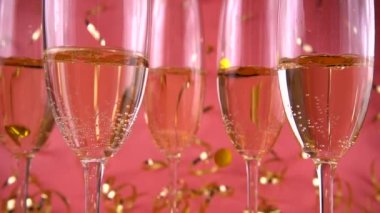 Pembe arka planda köpüklü şarapla bardaklara konfeti düşmesi. Yavaş çekim.