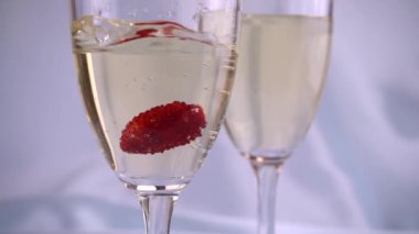 Mavi arka planda bir bardak köpüklü şarabın içine düşen çilekler. Yavaş çekim.