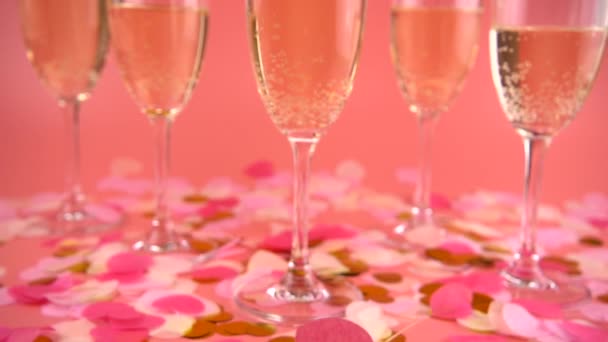 Falling Confetti Form Hearts Background Glasses Sparkling Wine Pink Background — Stockvideo