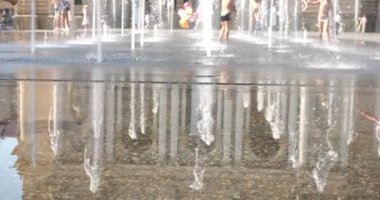 Children cool off in the jets of the fountain in the summer in the city. Slow motion. Out of focus.