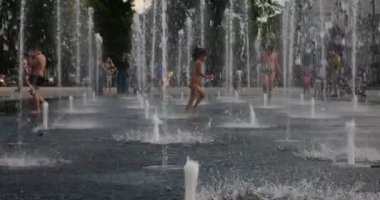 LVIV, UKRAINE - AUGUST 02, 2022: Children cool off in the jets of the fountain in the summer in the city. Slow motion.