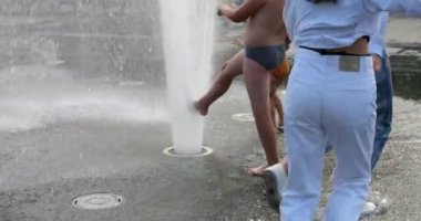 Children cool off in the jets of the fountain in the summer in the city. Slow motion.