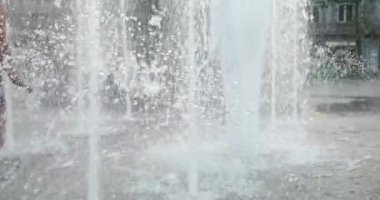 Children cool off in the jets of the fountain in the summer in the city. Slow motion.