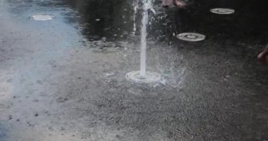Children cool off in the jets of the fountain in the summer in the city. Slow motion.