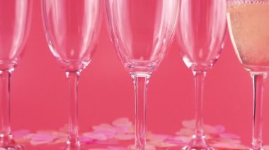 Köpüklü şarap, kalp şeklindeki konfetilerle pembe arka planda bardaklara dökülür..