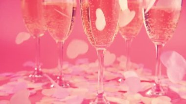 Pembe arka planda köpüklü şarapla arka planda kalp şeklinde konfeti düşmesi. Yavaş çekim.