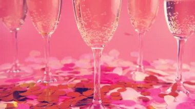 Pembe arka planda köpüklü şarapla bardakların arkasına konfeti düşmesi. Yavaş çekim.