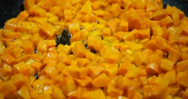 Pieces of carrots are fried in a pan.