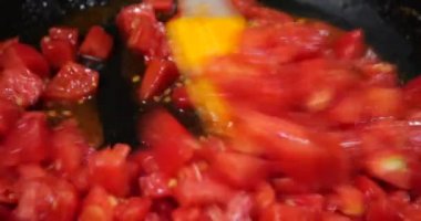 Pieces of tomatoes are fried in a pan.