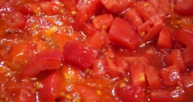 Pieces of tomatoes are fried in a pan.
