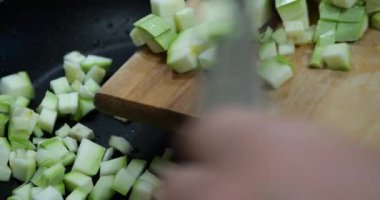 Sliced cubes of zucchini are poured into a frying pan.