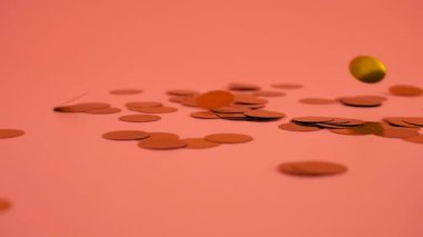 Falling confetti on a peach-pink background. Slow motion.