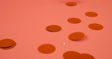 Falling confetti on a peach-pink background. Slow motion.