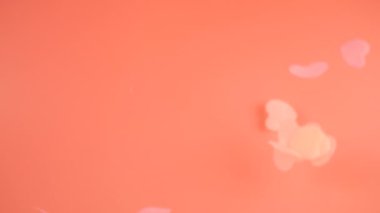 Falling confetti on a peach-pink background. Slow motion.