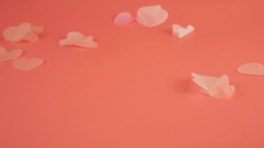 Falling confetti on a peach-pink background. Slow motion.