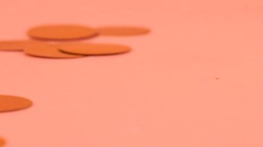Falling confetti on a peach-pink background. Slow motion.